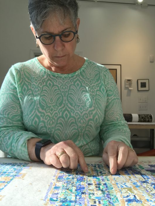 A woman in glasses is cutting paper with scissors.